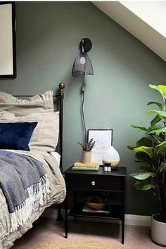 a bedroom with a bed, nightstand and plant on the floor in front of it