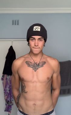 a shirtless man wearing a beanie standing in front of a closet with clothes hanging on the wall