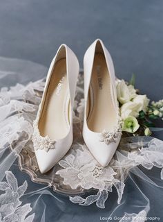 a pair of white high heels sitting on top of a wedding dress with flowers in the background