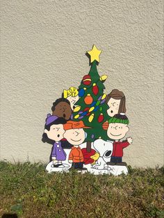 a charlie brown christmas tree with peanuts around it on the grass in front of a white wall