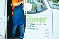 a man in an orange shirt standing next to a white truck with the words cloverr on it