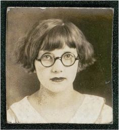 an old black and white photo of a woman with glasses on her face, looking at the camera