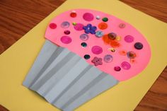 a cupcake made out of paper with buttons on the top and bottom, sitting on a piece of yellow paper