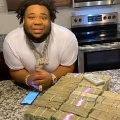 a man sitting at a kitchen counter with stacks of money in front of him and his cell phone