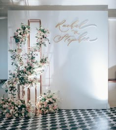 a white and gold wedding backdrop with flowers on the side, next to a black and white checkered floor