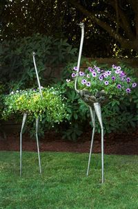 two metal birds are standing in the grass with purple flowers growing out of their legs