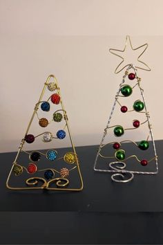 two christmas trees made out of metal and colored glass balls are sitting on a table