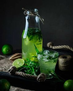 a glass pitcher filled with green liquid next to limes and twined twine