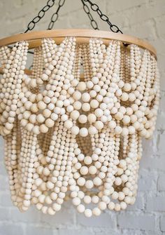 a chandelier made out of white beads hanging from a chain on a brick wall