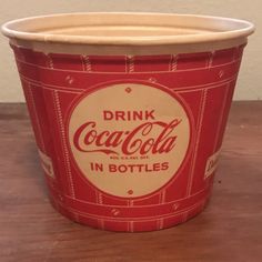 a red and white cup sitting on top of a wooden table next to a wall