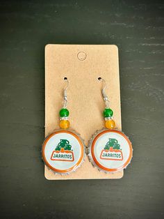 two bottle caps with green and orange beads are on the earwires of earrings