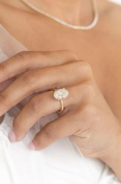 a close up of a person's hand with a ring on their finger, wearing a white dress