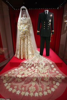 a wedding dress and suit on display in a glass case with red curtains behind it