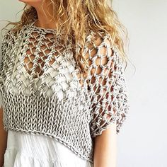 a woman with long hair wearing a crocheted sweater and white dress standing in front of a wall