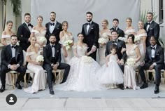 a large group of people in formal wear posing for a wedding photo with the bride and groom