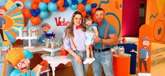 a man and woman holding a child in front of a cake table with decorations on it