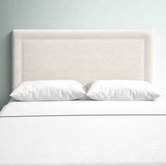 a white bed with two pillows on it's headboard and one is turned down