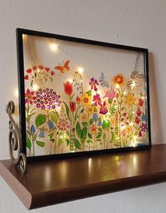 an art piece with flowers and butterflies is displayed on a shelf next to a pair of scissors