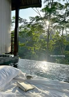 the sun shines brightly through the trees and water in front of a bed with white sheets on it