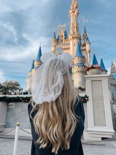 a woman with long blonde hair standing in front of a castle wearing a white veil