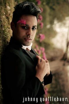 a man in a tuxedo is posing for a photo with flowers behind him