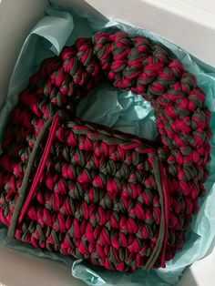 a red and green handbag sitting inside of a white box on top of a table