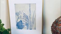 a blue and white painting sitting on top of a table next to a potted plant