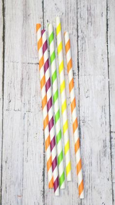 four multicolored striped paper drinking straws on a white wooden table with one orange, one green and one pink