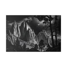 black and white photograph of mountains with trees in the foreground, dark clouds overhead