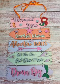 mermaid name tags are hanging on a wooden board with orange ribbon around the neck and bottom