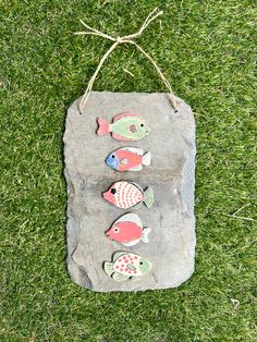 a rock with three fish on it sitting in the grass next to a string and two strings