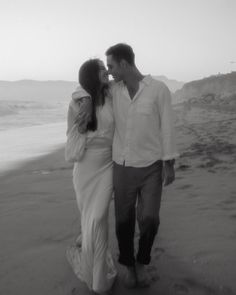 a man and woman walking on the beach next to each other with water in the background