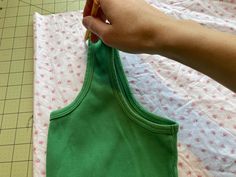 someone is cutting out the back of a green tank top with a pair of scissors