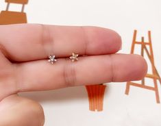 a person's hand holding two tiny white diamond studs