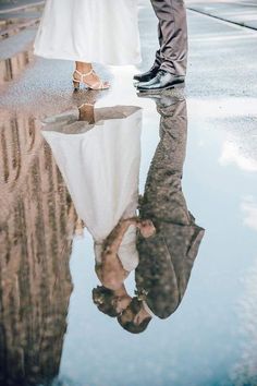 a man and woman standing next to each other in the rain with their reflection on the ground