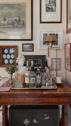 a bar cart with liquor bottles and glasses on it in front of framed pictures above