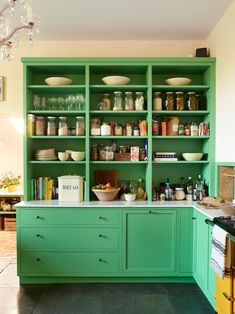 a kitchen with green cabinets and lots of food on the counter top in front of a chandelier