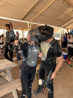 two people in wetsuits and helmets standing near a picnic table with other people