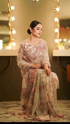 a woman sitting in front of a mirror wearing a dress with flowers on the skirt