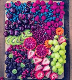 an assortment of fresh fruits and vegetables laid out on a cutting board, including grapes, raspberries, kiwis, cherries, strawberries, and more