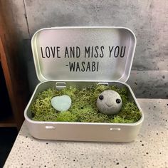 two rocks in a tin with moss and the words love and miss you wasabi