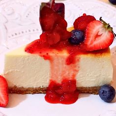 a piece of cheesecake with strawberries and blueberries on the top is sitting on a plate