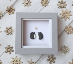 two black and white earrings in a shadow box surrounded by gold snowflakes on the floor