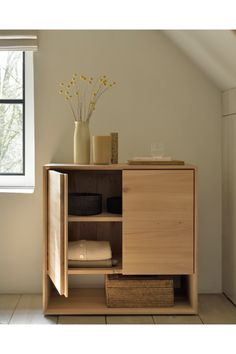 a wooden cabinet with baskets and vases on top in a room next to a window