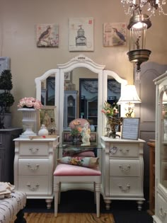 a white dresser sitting next to a mirror on top of a wooden floor covered in furniture