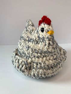 a knitted chicken sitting on top of a white table next to a black and white wall