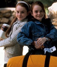 two girls are carrying a duffel bag and smiling at the camera while standing next to each other