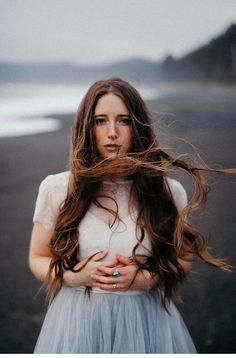 a woman with long hair standing on the beach