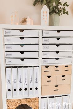 a white cabinet filled with lots of drawers next to a potted plant on top of a table