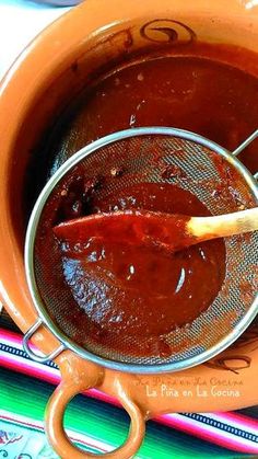 a wooden spoon in a pot filled with red sauce on top of a colorful table cloth